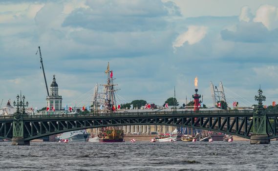 Russia, St. Petersburg, 28 July 2022: Trinity Bridge in the foreground, many ancient frigates stand at the lit Rostral columns on the eve of the celebration of the Day of the Navy, the barque Poltava. High quality photo