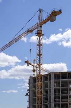 A working construction tower crane against a cloudy sky on a sunny day. The concept of urban development and construction. Industrial background. Crane engineering, construction industry tool