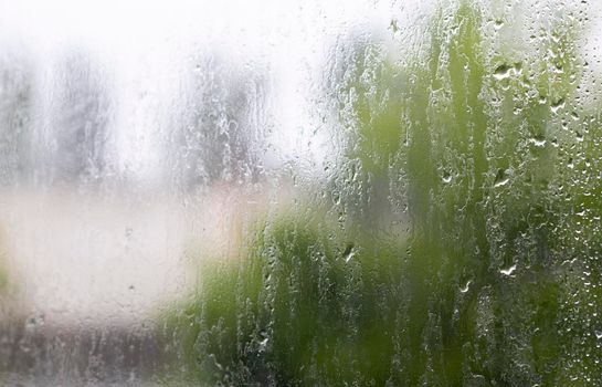 Heavy rain. Raindrops on the window glass on a summer day. Selective focus, shallow depth of field. Drops of water fall on a wet window. Glass full of drops during a downpour