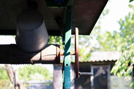 A well with a bucket in a European village. Sunny day. Metal bucket for a water well. Detail of a well with a tin bucket in the countryside. Decorating the garden with vintage items