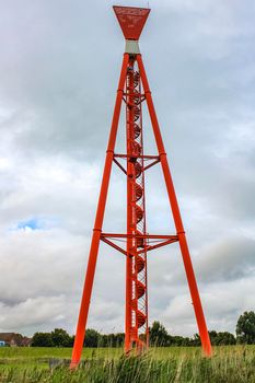 Industrial area cranes and red tower lighthouse with beautiful grassland and dike dyke nature seascape panorama in Imsum Geestland Cuxhaven Lower Saxony Germany.