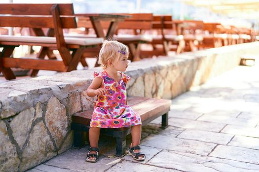 Little girl sits on a bench near an open-air restaurant. High quality photo