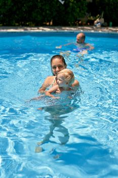 Mom with a little girl swims in a pool with turquoise water. High quality photo