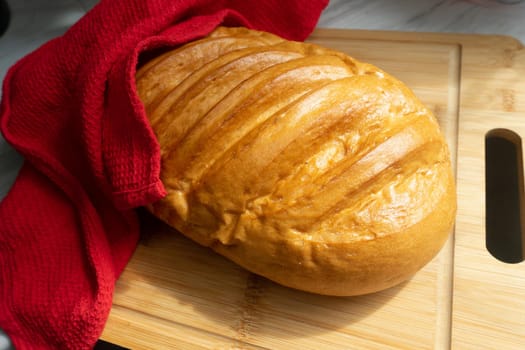 Fresh homemade loaf covered with a red towel lies on a wooden board. High quality photo