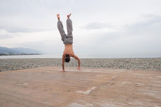 Shirtless caucasian man doing backflip on pebble beach