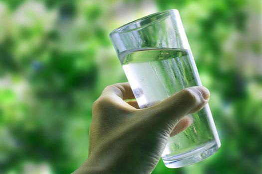 A glass of water in a hand close-up on a natural green background outdoors..