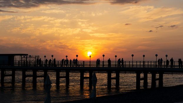 LAZAREVSKOE, SOCHI, RUSSIA - MAY, 26, 2021: Orange saturated sunset with silhouettes of people on the background of the sun.