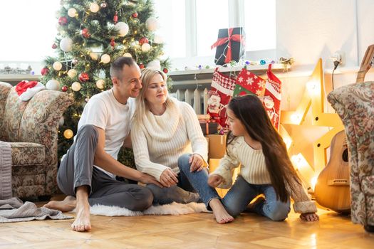 Christmas Family. Happiness. Portrait of dad, mom and daughter sitting at home near the Christmas tree.