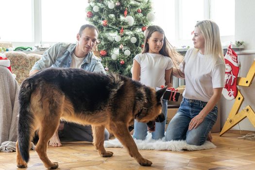 smiling family and daughter with dog sitting near christmas tree with gifts.