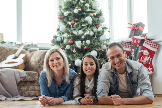 Christmas Family. Happiness. Portrait of dad, mom and daughter at home near the Christmas tree, all are smiling.