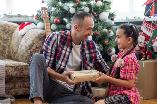 Little four year girl with her dad in living room decorated by Christmas tree and present gift box, the light give cozy atmosphere. New Year and merry xmas daughter and father concept