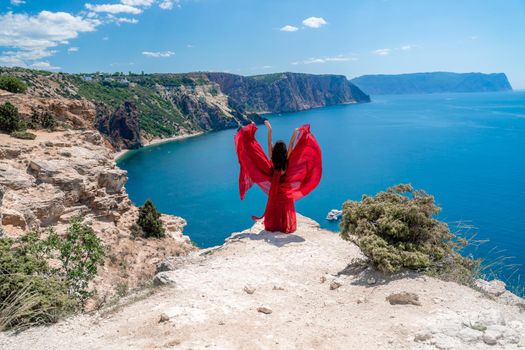 A woman in a red flying dress fluttering in the wind, against the backdrop of the sea