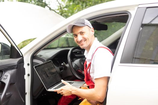 Mechanic with laptop near car engine. Modern car diagnostic program on screen. Car service concept.