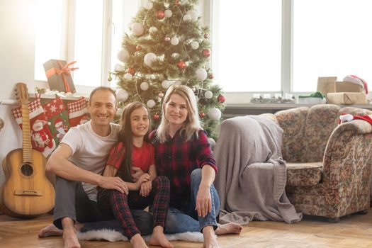 Merry Christmas and Happy New Year. Happy family is waiting for the New Year while sitting near beautiful Christmas tree at home.