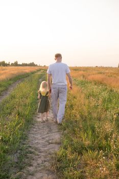 Dad and his blonde daughter are walking and having fun in a chamomile field. The concept of Father's Day, family and nature walks.