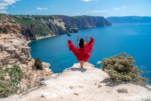 A woman in a red flying dress fluttering in the wind, against the backdrop of the sea