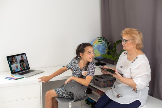 Happy grandmother and her granddaughter having video chat via laptop together at home