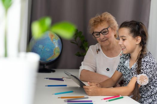 Portrait of smiling little girl teaching grandmother using digital tablet and internet in cozy home.