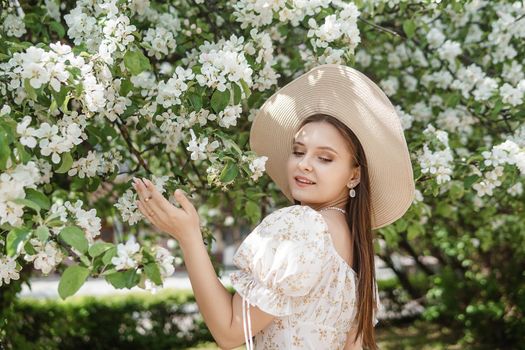 An attractive long-haired woman walks in the spring in the park of blooming apple trees. Spring portrait of a woman