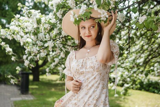 An attractive long-haired woman walks in the spring in the park of blooming apple trees. Spring portrait of a woman