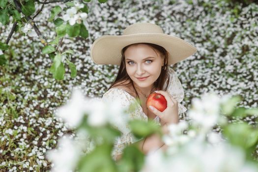 An attractive long-haired woman walks in the spring in the park of blooming apple trees. Spring portrait of a woman