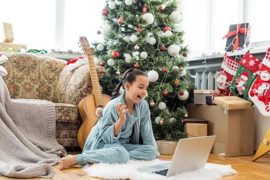 Christmas tree in a large living room. Little girl plays near the Christmas tree. A girl with a laptop communicates with friends