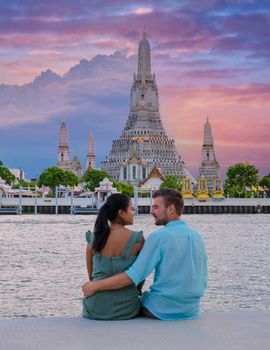 Wat Arun temple Bangkok Thailand, Temple of Dawn, Buddhist temple alongside Chao Phraya River.Beautiful Wat Arun at dusk evening sunset, couple Asian woman and European men watching sunset