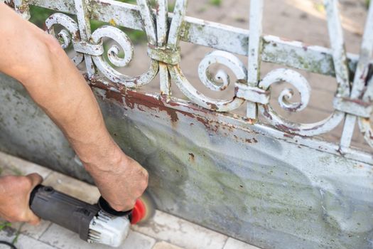 Male worker while peeling off old paint of fence.