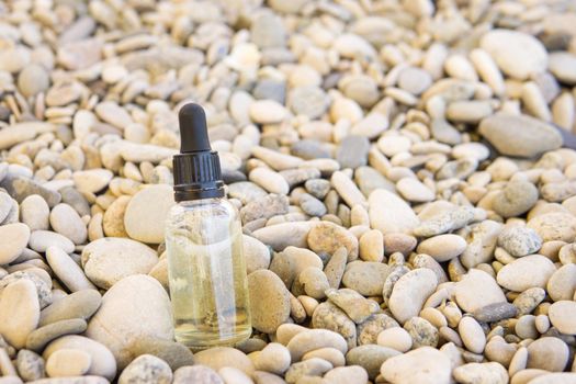 Cosmetic serum for the skin in a glass bottle. A bottle with an eyedropper on a pebble beach by the sea. Essences for skin care on the background of stones. The concept of natural cosmetics and SPA products.