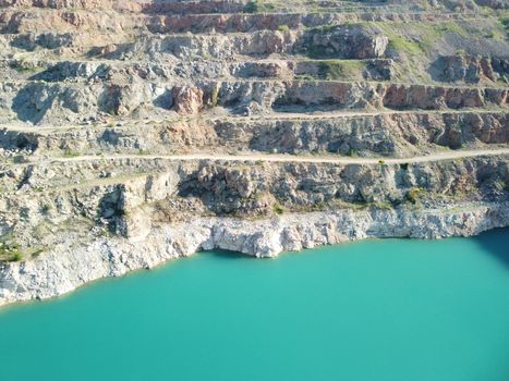 Flight over the turquoise surface of the lake in the center of the quarry. Industrial of opencast mining quarry with flooded bottom. Small lake in the shape of a heart