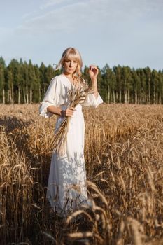 A blonde woman in a long white dress walks in a wheat field. The concept of a wedding and walking in nature.