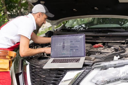 Mechanic man close up using laptop computer examining tuning fixing repairing car engine automobile vehicle parts using tools equipment in workshop garage support service in overall work uniform.