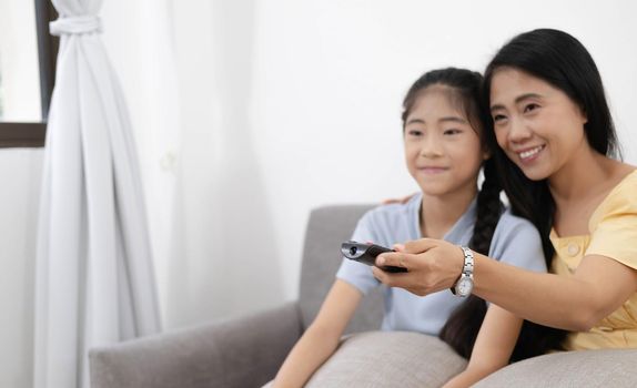 Happy asian parents sit on comfortable couch in living room with little kids watch TV enjoy home weekend enjoying movie.