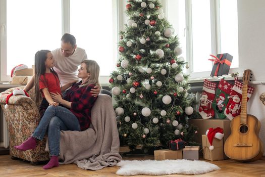 Merry Christmas and Happy New Year. Happy family is waiting for the New Year while sitting near beautiful Christmas tree at home.