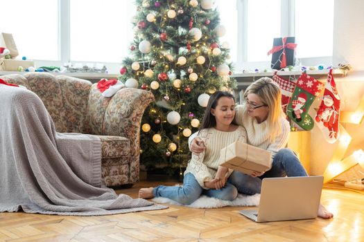 cheerful teenage girl and mother celebrating christmas at home and communicating online.