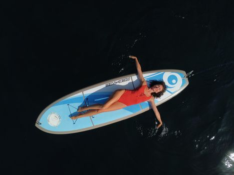 Young attractive brunette woman in red swimsuit, swimming on kayak around volcanic rocks, like in Iceland. Back view. Christmas holiday vacation and travel concept.