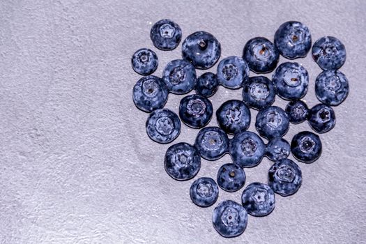 The heart is made of fresh, healthy blueberries on a gray table. Farm vitamins in summer.