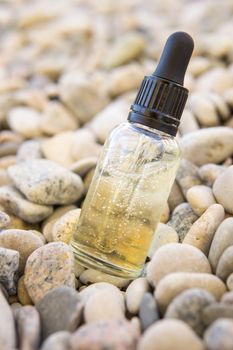 Cosmetic serum for the skin in a glass bottle. A bottle with an eyedropper on a pebble beach by the sea. Essences for skin care on the background of stones. The concept of natural cosmetics and SPA products.