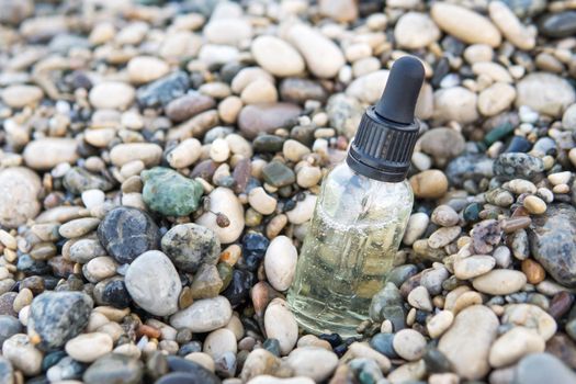 Cosmetic serum for the skin in a glass bottle. A bottle with an eyedropper on a pebble beach by the sea. Essences for skin care on the background of stones. The concept of natural cosmetics and SPA products.