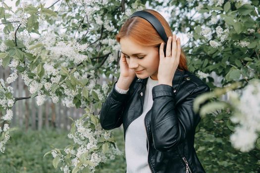 A red-haired teenage girl listens to music in headphones, configured via the phone. The time of spring flowering of cherry orchards