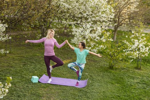 Family Mother teacher training yoga child daughter on a yoga mat at home garden. Family outdoors. Parent with child spends time together. exercise at home concept and new normal