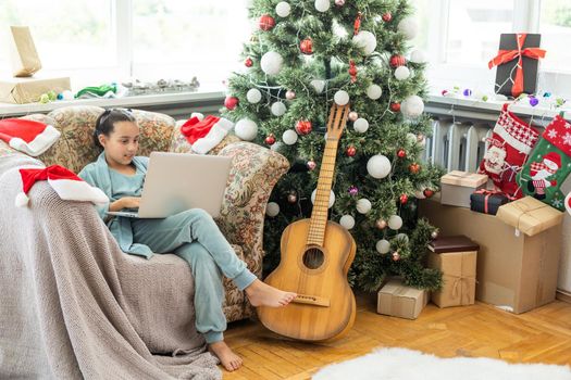 winter holidays, technology and children concept - little student girl with laptop computer at home over christmas tree background