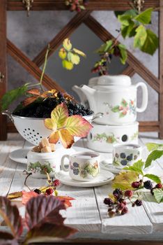 fruit tea with ripe blackberries, vintage still life with beautiful retro set and colander full of berries on the table, summer food, cups with floral-berry pattern, High quality photo