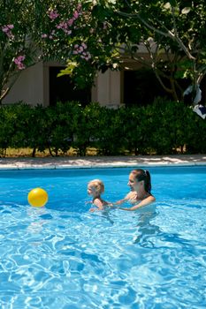 Mom with a small baby play with a ball in the pool. High quality photo