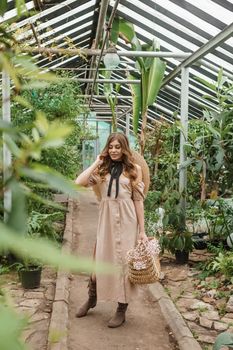 A beautiful young woman takes care of plants in a greenhouse. The concept of gardening and an eco-friendly lifestyle.