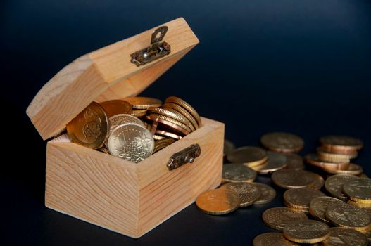Scattered gold coins with treasure chest on dark background cover. Copy space