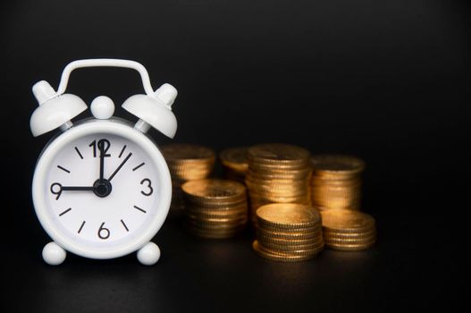 White alarm clock with gold coins isolated on dark background. Copy space and business concept.
