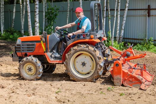A man on a mini-excavator levels a piece of land, loosens the soil