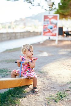 Little girl sits on the teeter-totter in the playground. High quality photo