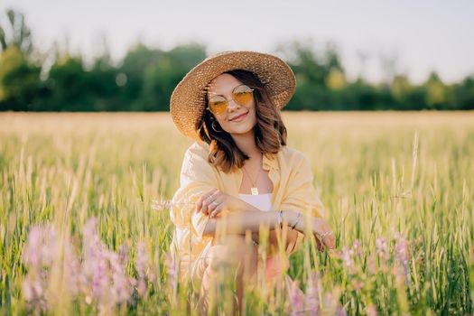 Portrait of rural stylish woman in straw hat posing in fresh wheat field. Grass background. Amazing nature, lifestyle, farmland, growing cereal plants. High quality photo